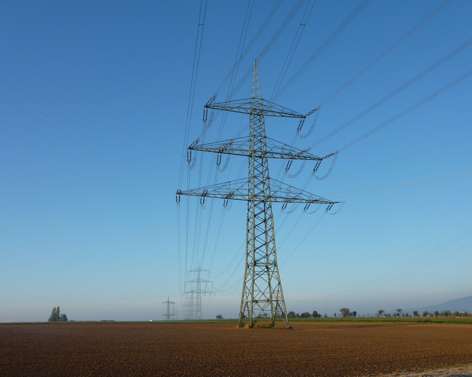 Hoogspanningsleidingen op een toren in een open veld tegen een helderblauwe lucht.