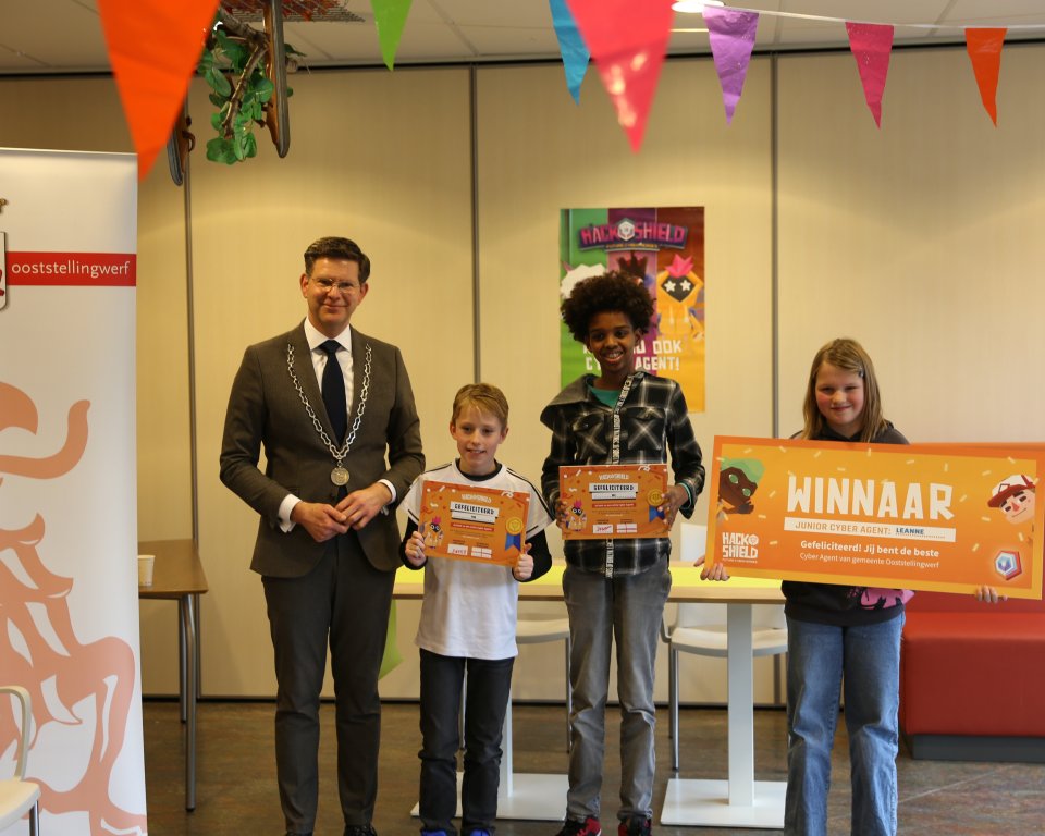 Burgemeester Jack Werkman staat samen met topscoorder Pim, Mo en Leanne op de foto. De kinderen houden een certificaat omhoog van het online spel HackShield