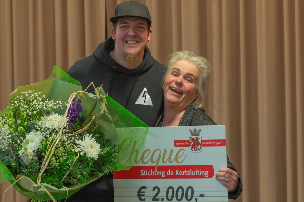 Steve Bergsma en Jolanda Ruitenbeek van Stichting de Kortsluiting houden een cheque van 2000 euro en een bos bloemen omhoog