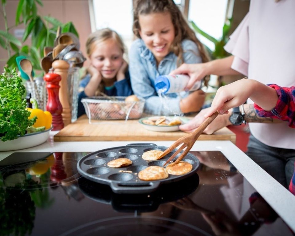 Kinderen kijken toe hoe poffertjes worden gebakken