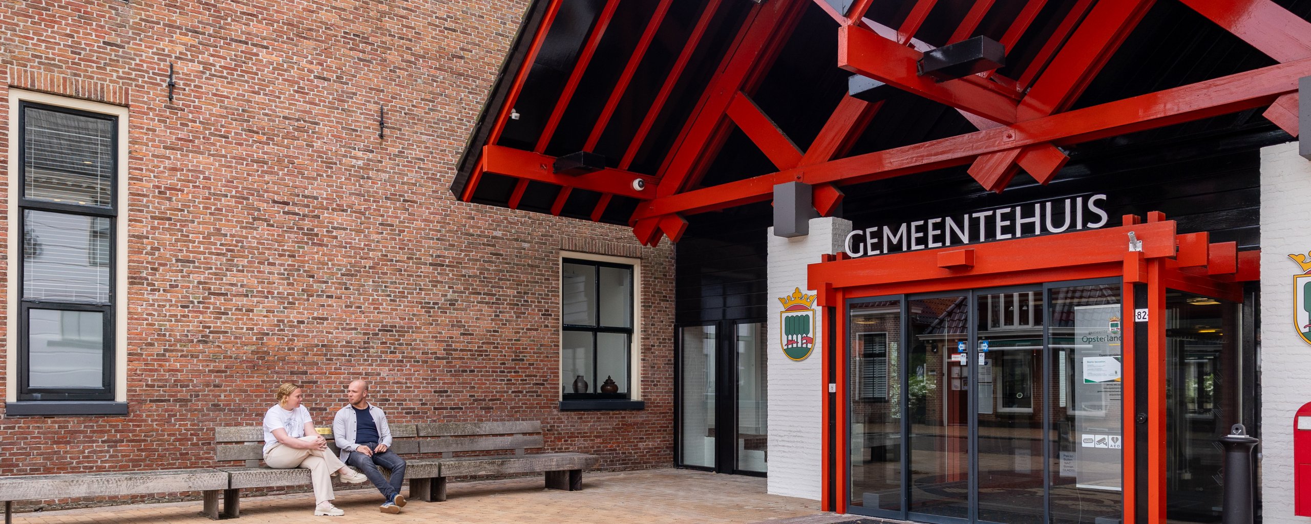 Ingang van het gemeentehuis met twee mensen op een bankje