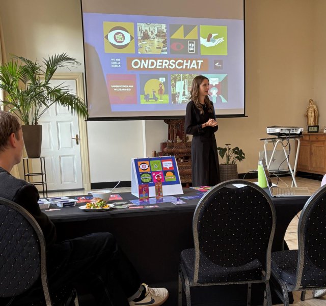 Presentatie van de toolkit, genaamd onderschat, vrouw geeft presentatie met beamer, toehoorder aan tafel