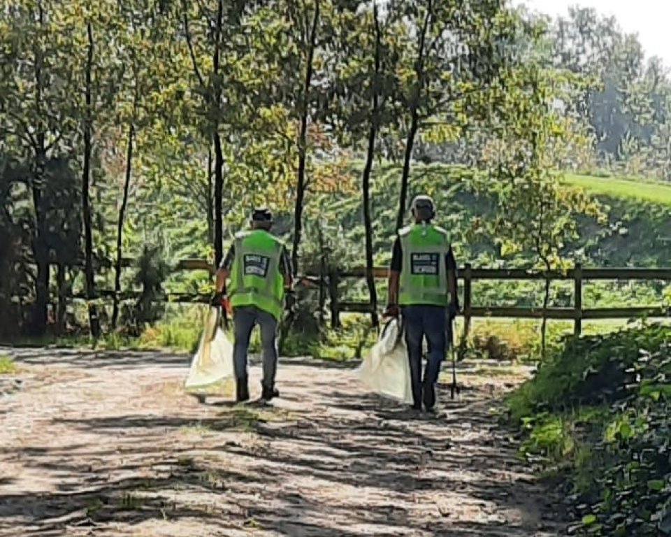 Twee mannen lopen met een afvalzak door het bos