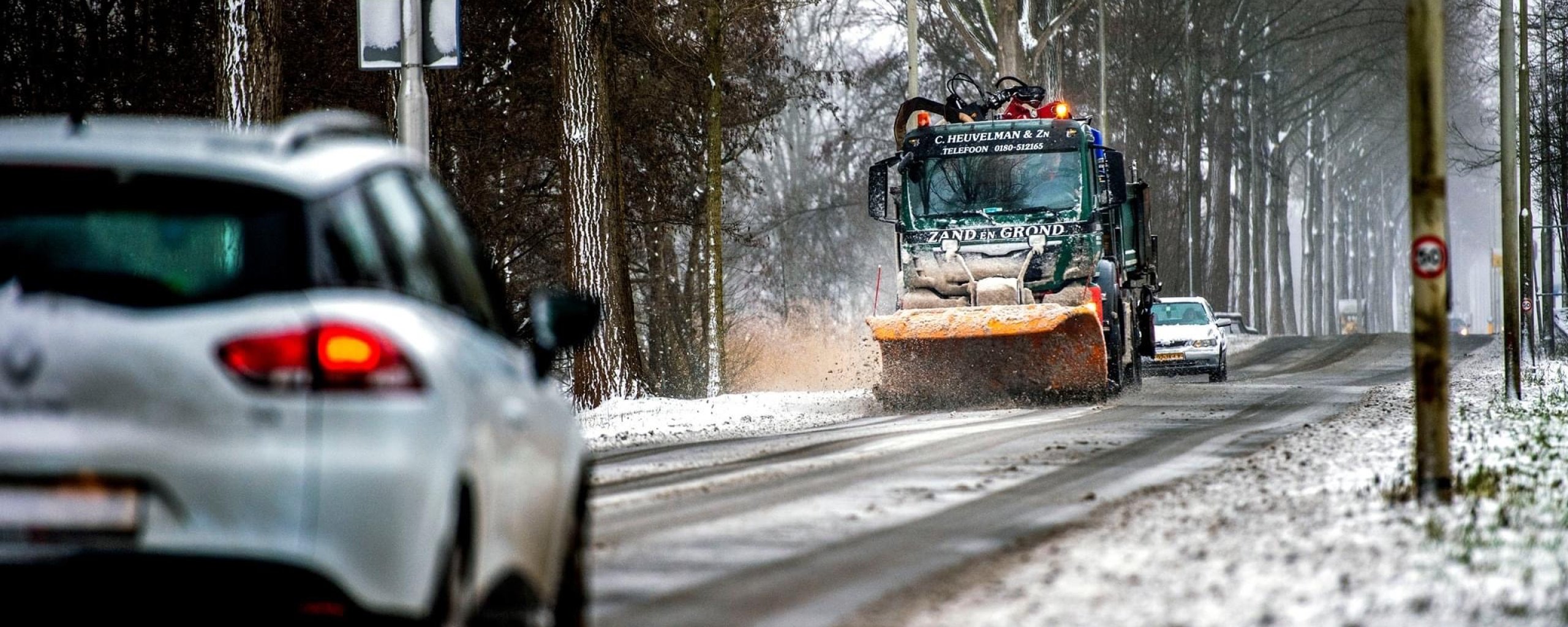 Foto van een strooiwagen op een besneeuwde weg