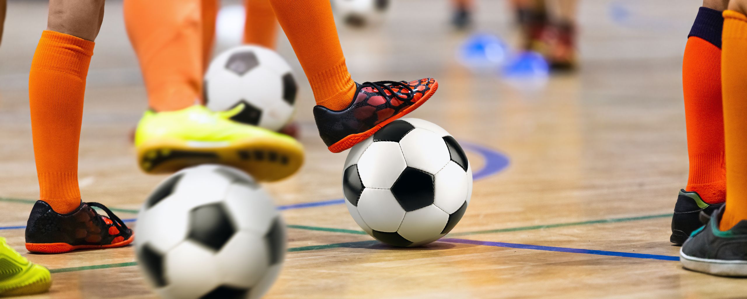 Kinderen in een sportzaal met een voetbal onder hun voet.