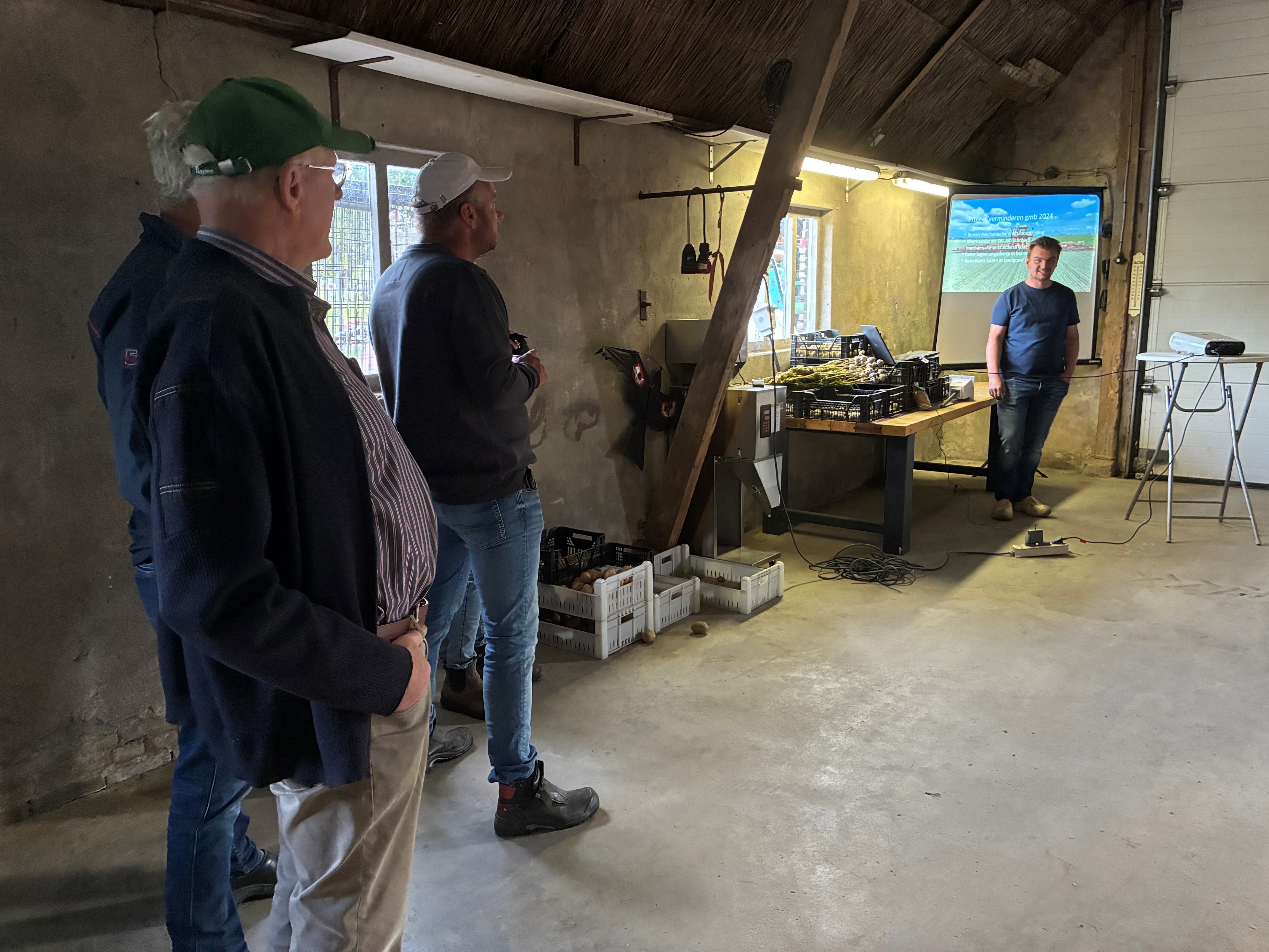 Een aantal mensen staan in een schuur te overleggen.