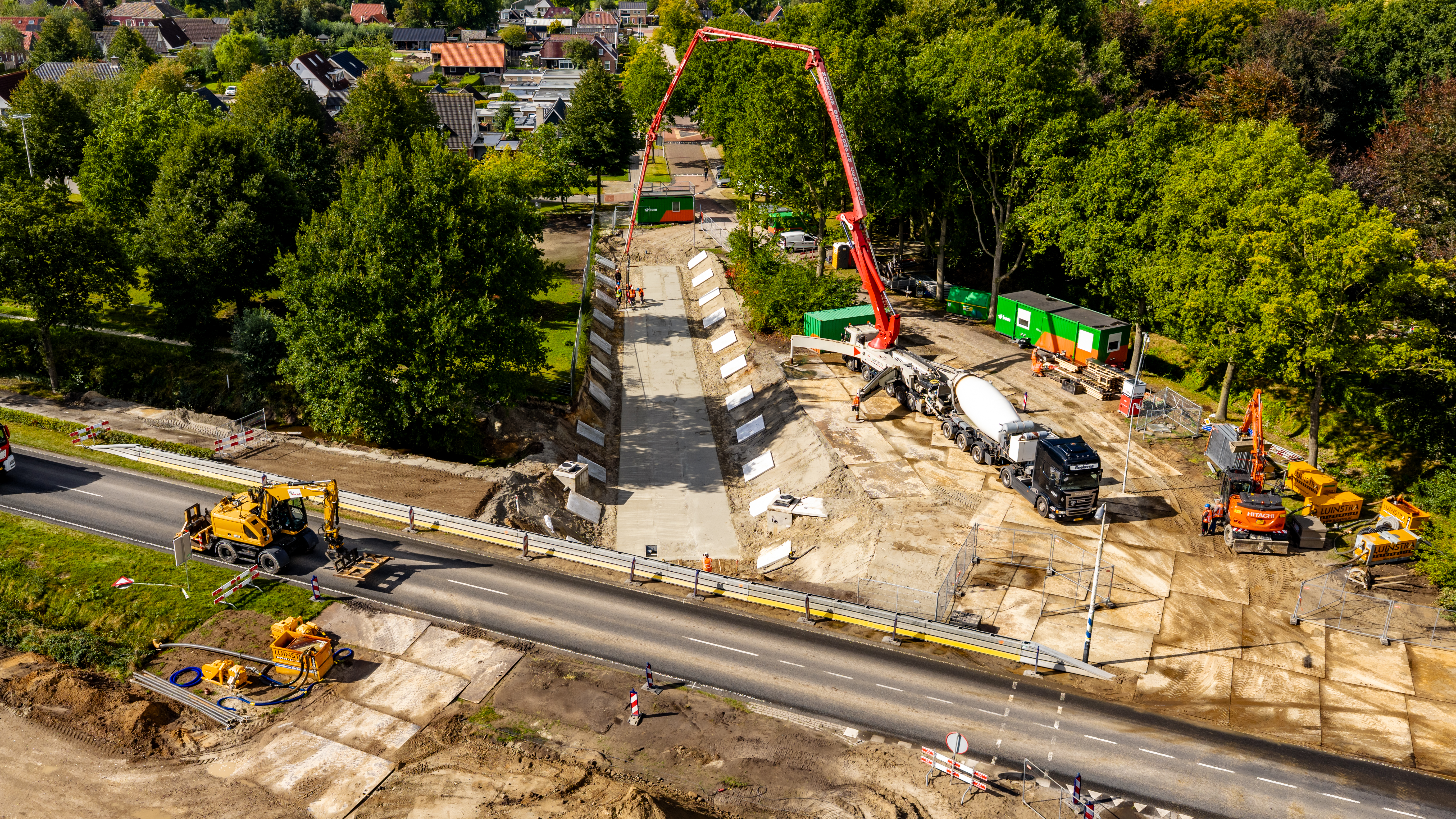 Een kraan is bezig met het vlak maken van het fietspad voor de fietstunnel die onder de weg door gebouwd wordt.