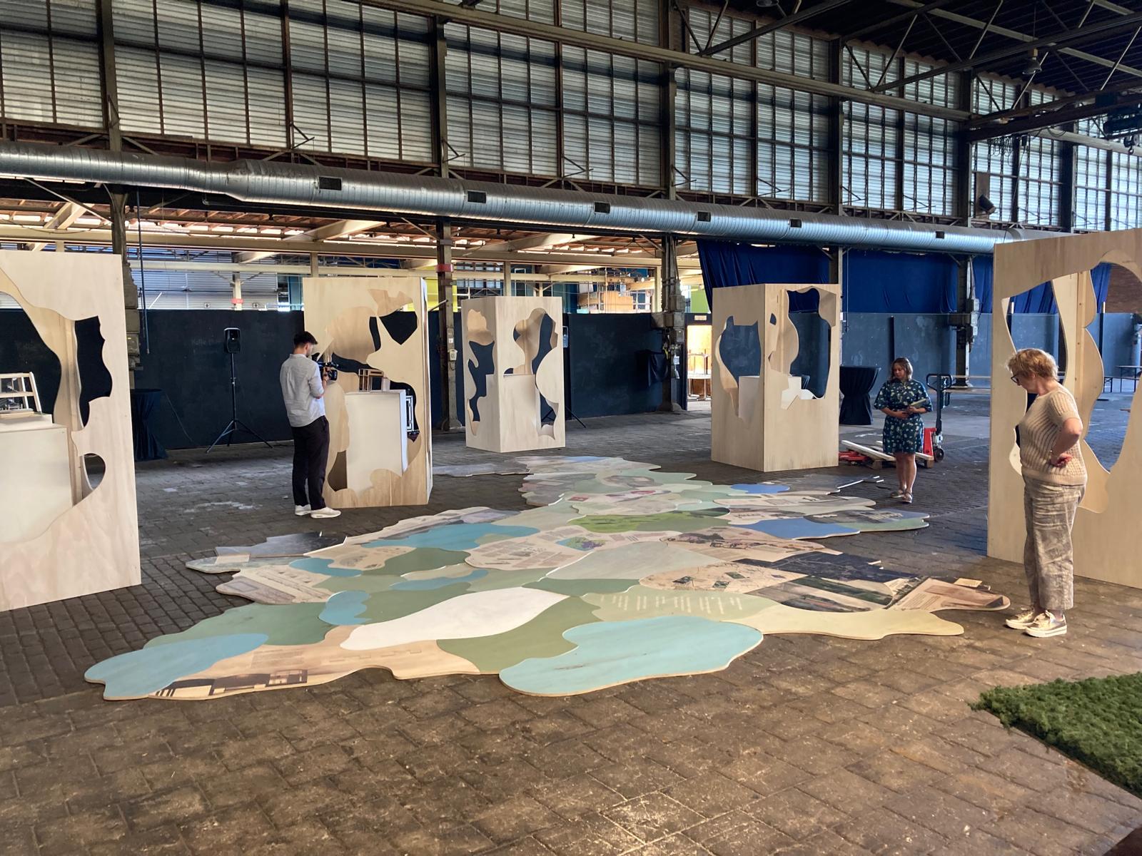 Een expositie van kartonnen dozen waar werelddelen in uitgesneden zijn. De uitsneden liggen op de grond.