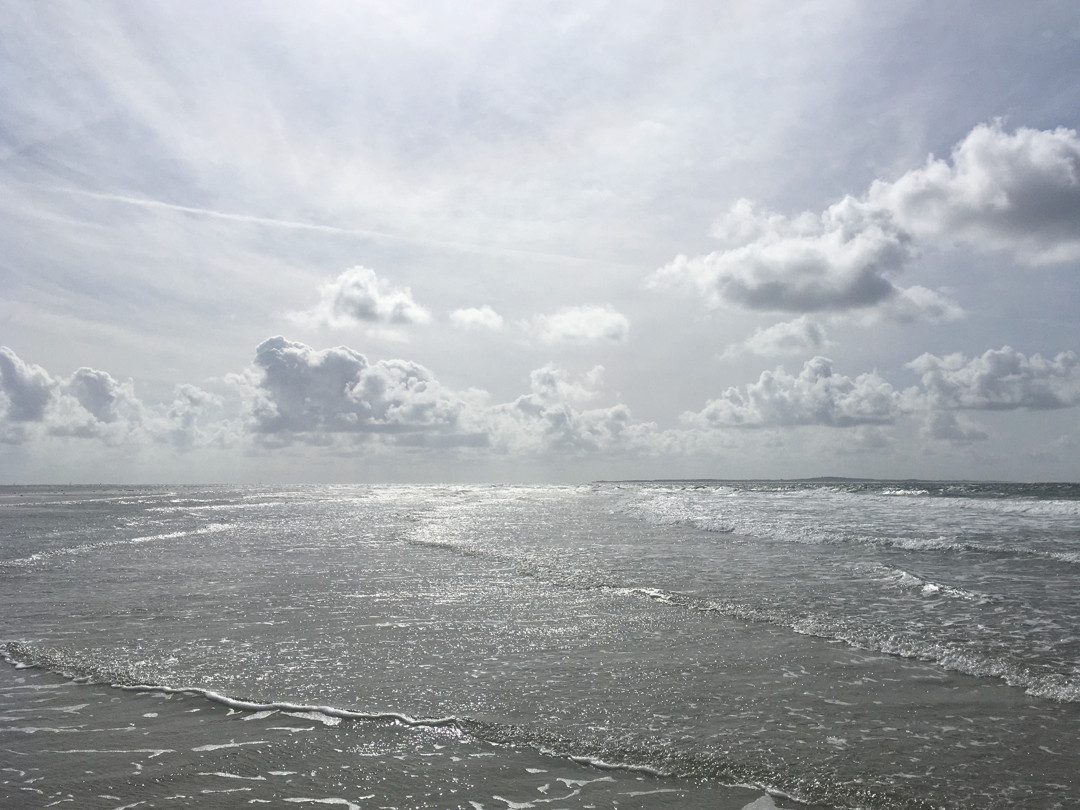 De zee met een bewolkte lucht erboven. Dit alles in een nazomers zonnetje.