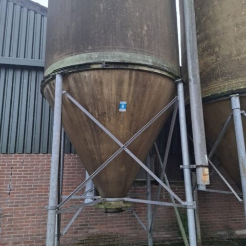 Een silo staat voor een stal op een betonnen vloer.