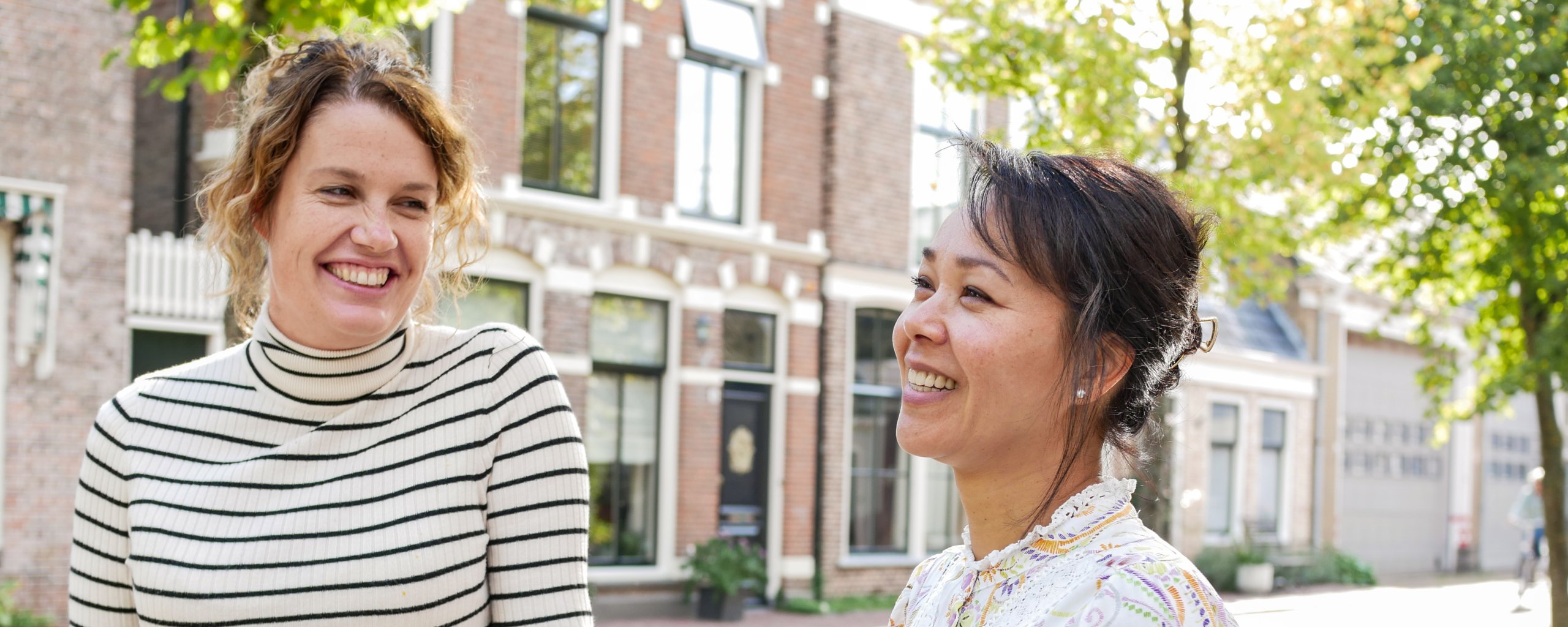 Twee personen staan buiten in de zon te lachen.