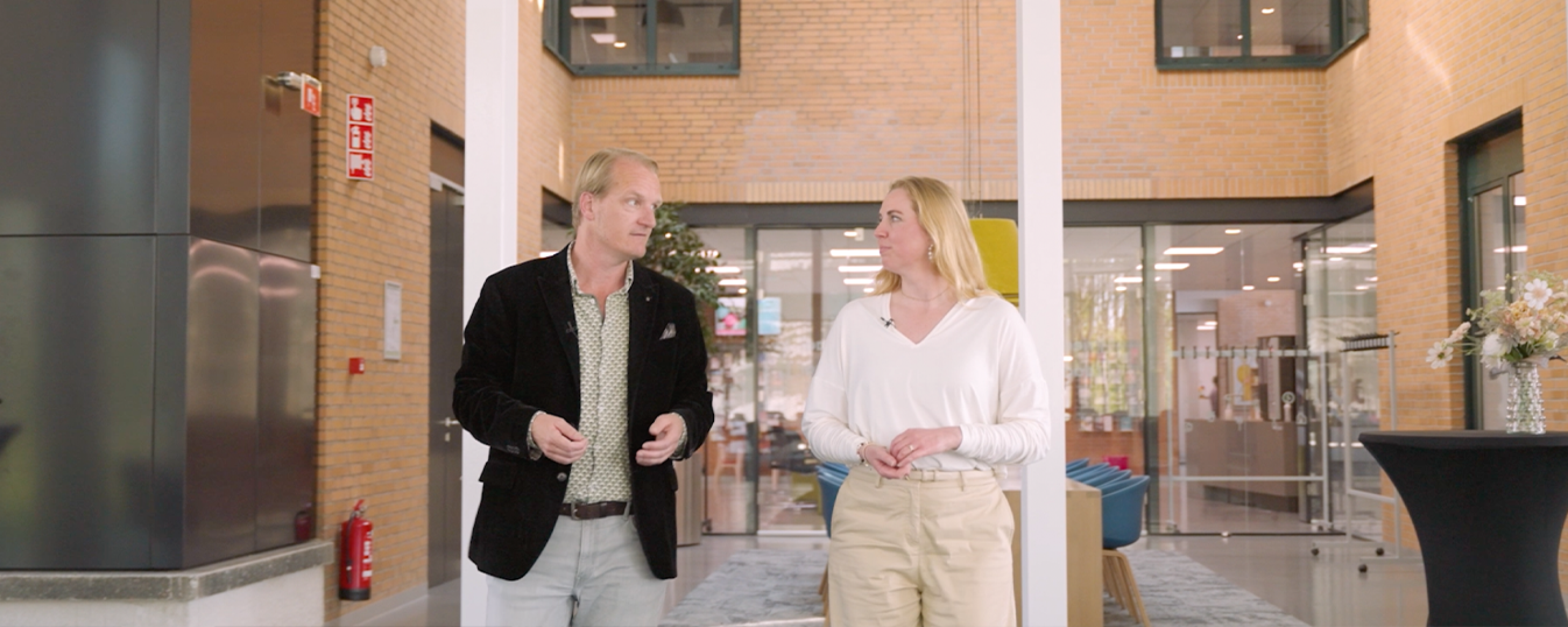 Een man en vrouw lopen al pratend door de hal van een gebouw