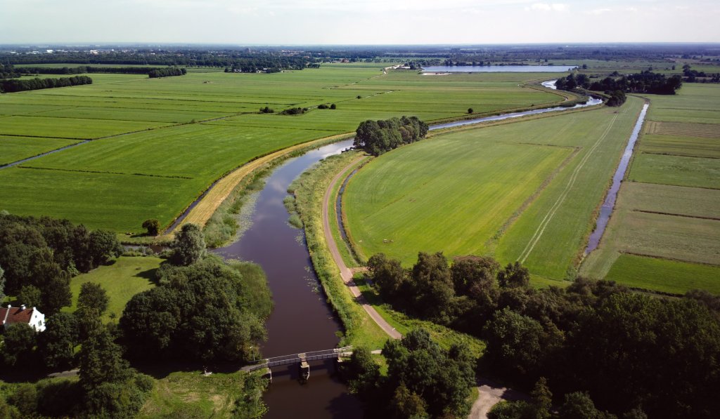 Landschap waar een brede vaart door heel loopt en hier en daar staan bomen.