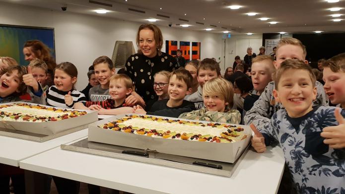 Gedeputeerde Sietske Poepjes poseert met twee grote taarten met daar omheen vrolijke kinderen