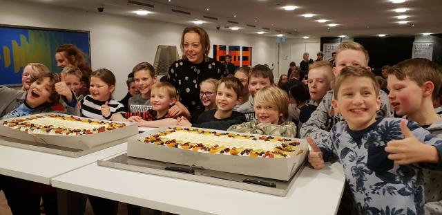 Gedeputeerde Sietske Poepjes poseert met twee grote taarten met daar omheen vrolijke kinderen