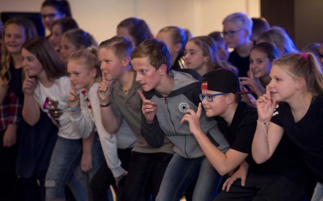 Een groep kinderen op het toneel die allemaal met de vinger voor de mond, mondje dicht doen.