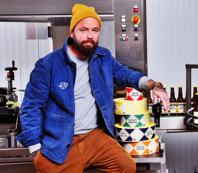 Sjoerd Kooistra zit met gele muts en blauw jasje op een machine met naast hem allemaal rollen stickers