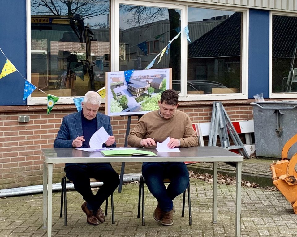wethouder en aannemer tekenen de overeenkomst aan een tafel voor de oude werf