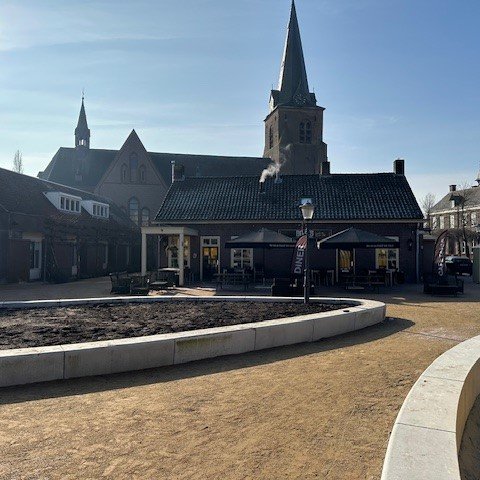 Het dorpsplein met de banken en plantsoenen, de kerk op de achtergrond