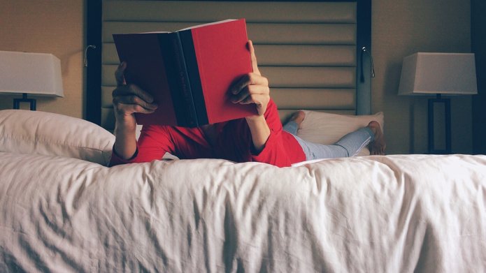 Een kind ligt met een boek voor het gezicht op bed te lezen.