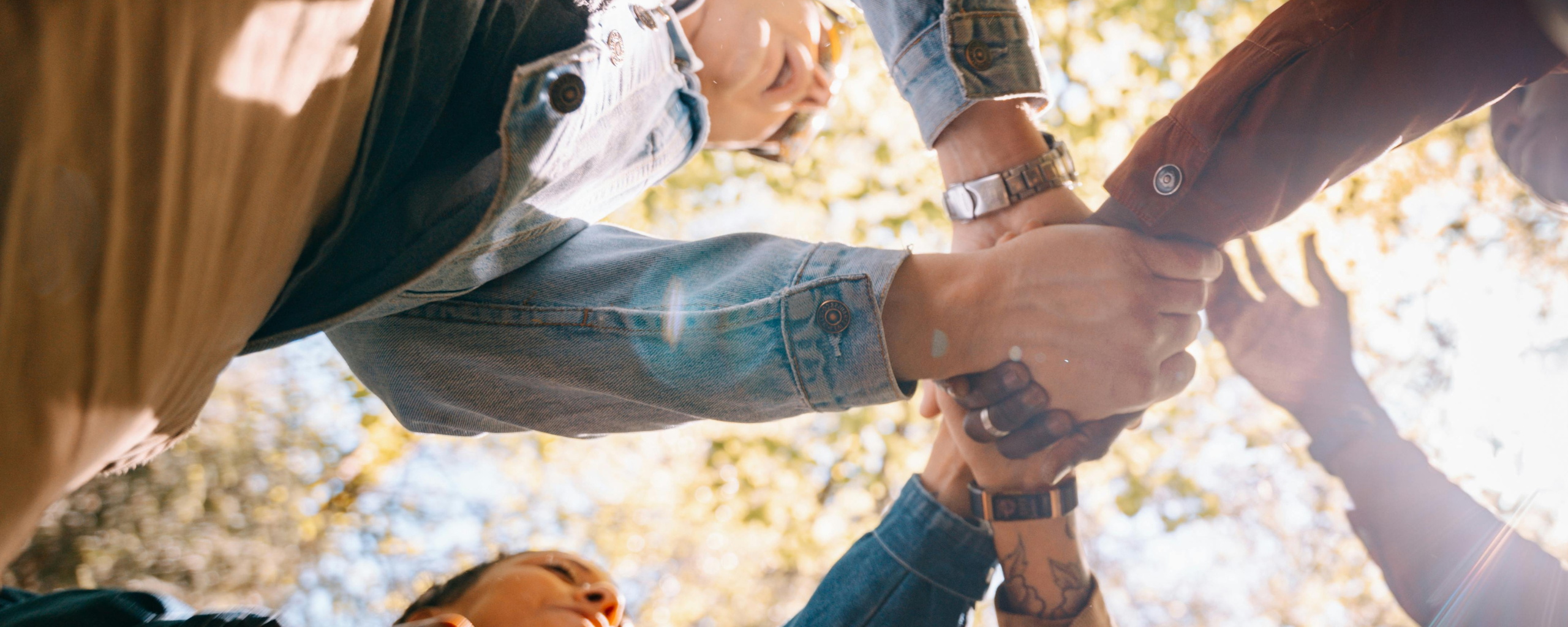 Handen zijn in ineen geslagen. Op de achtergrond schijnt de zon door bladeren.
