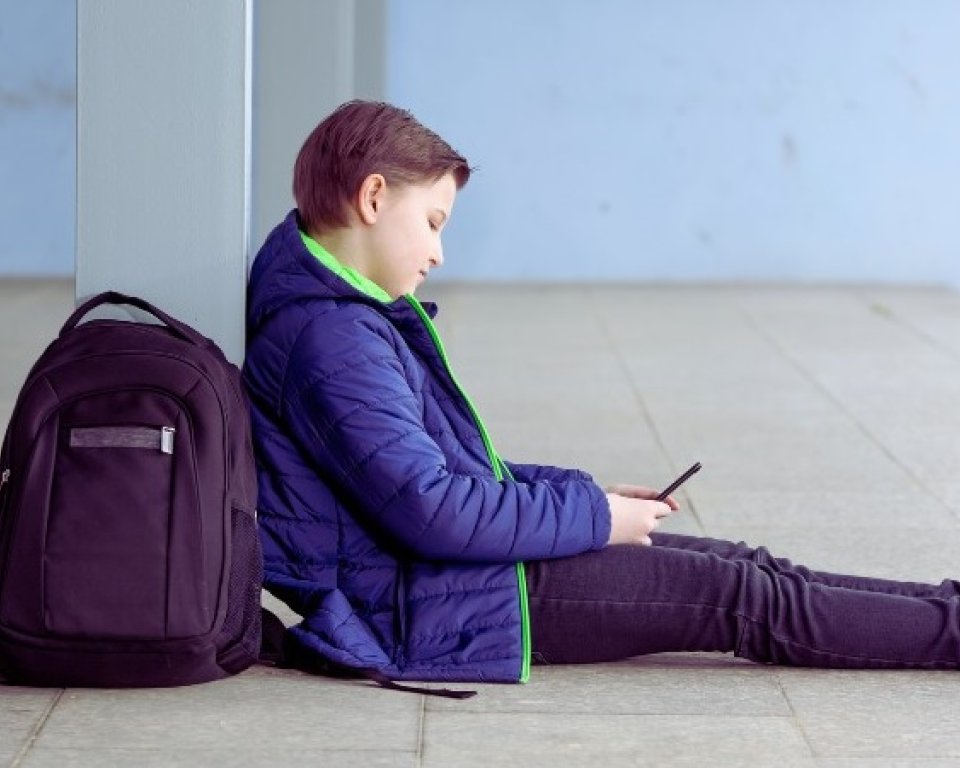 jongen zit tegen pilaar met rugzak