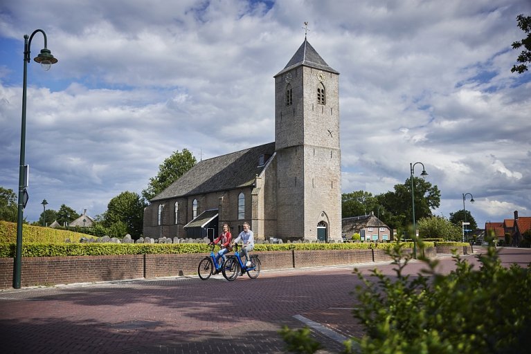 Man en vrouw op de fiets op de Oude Rijksweg ter hoogte van de kerk in Rouveen