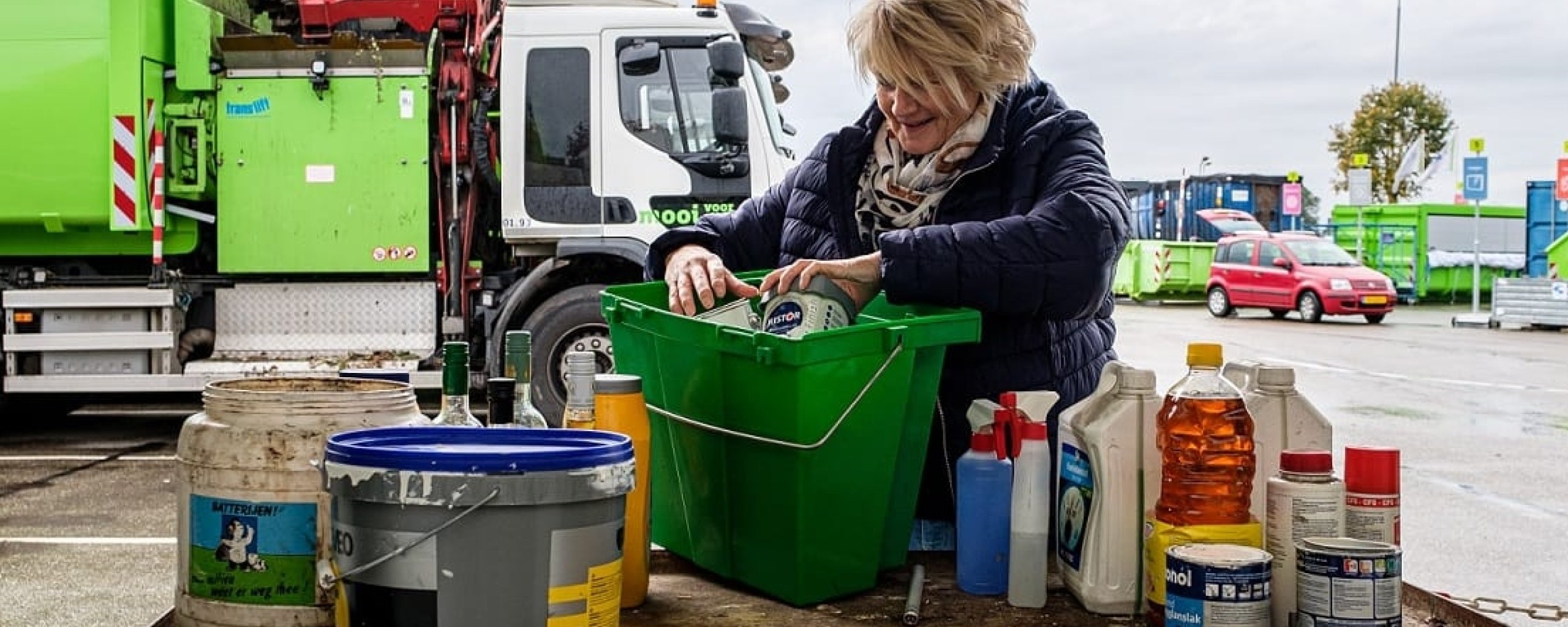 Vrouw haalt klein chemisch afval uit haar groene kca-emmer