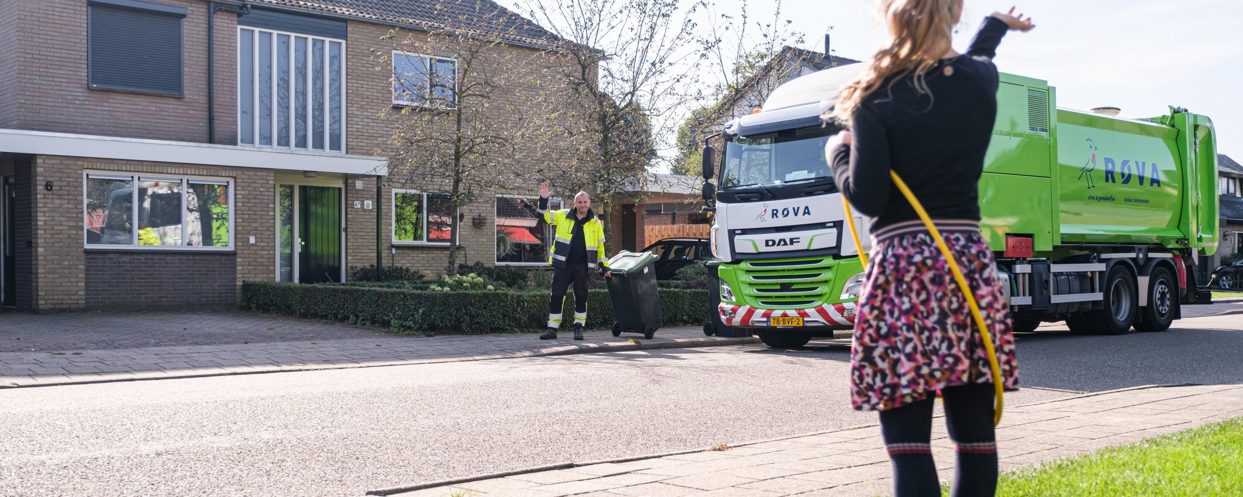 Meisje zwaait naar een ROVA-medewerker die een container heeft geleegd