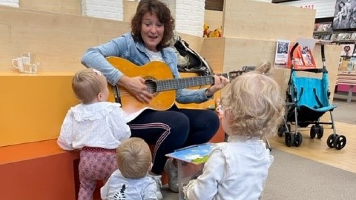 Vrouw met een gitaar, 3 kindjes kijken naar haar