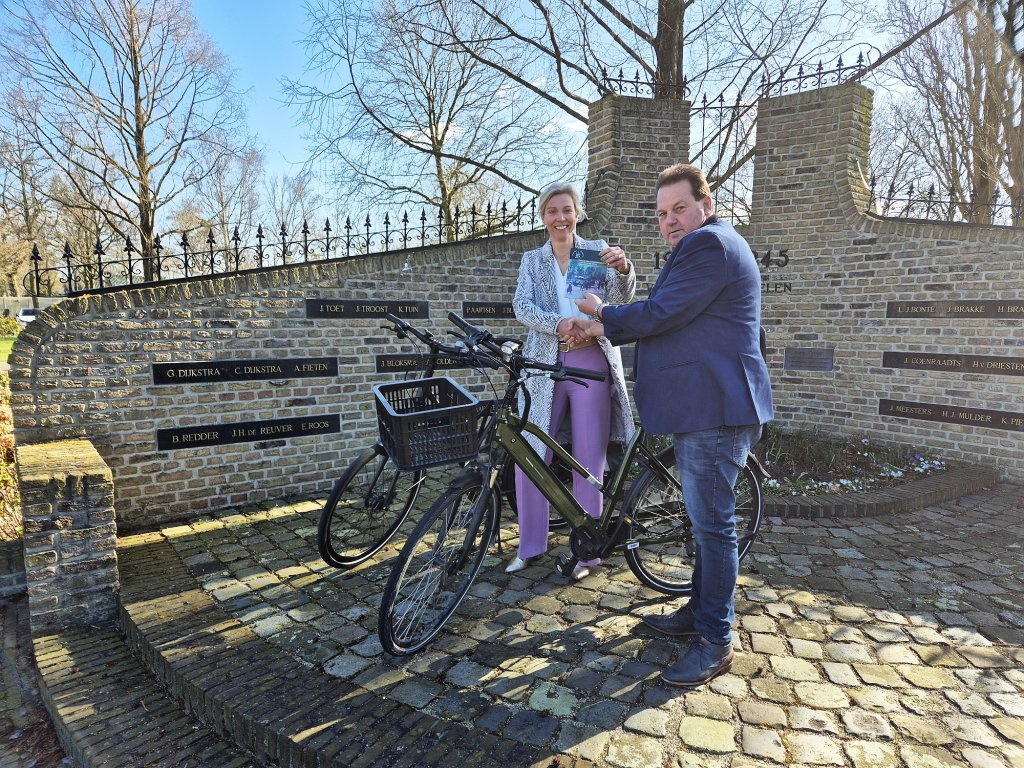 Wethouder Herriët Brinkman en voorzitter Henk Koobs van de Historische Vereniging Staphorst, beiden met een fiets voor het oorlogsmonument in Staphorst, presenteren de fietsroutes.