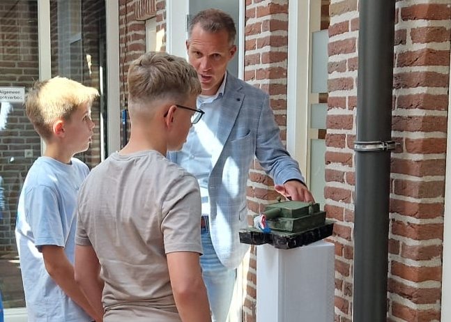 Wethouder bus met 2 kinderen bij een van de kunstwerken: een tank.