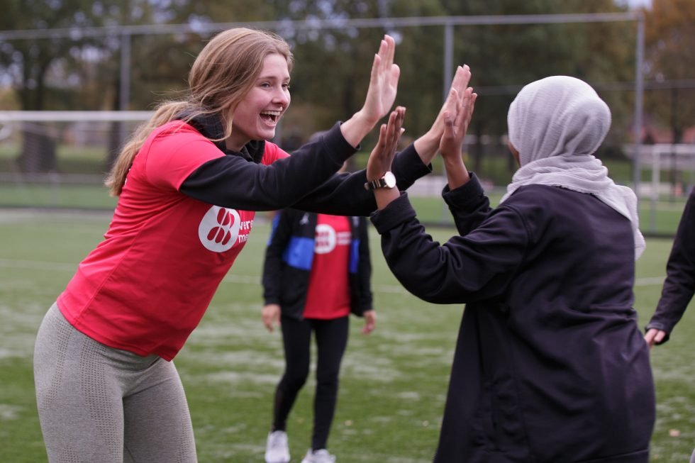 Op een sportveld geven een blond meisje en gesluierde persoon elkaar een high five.
