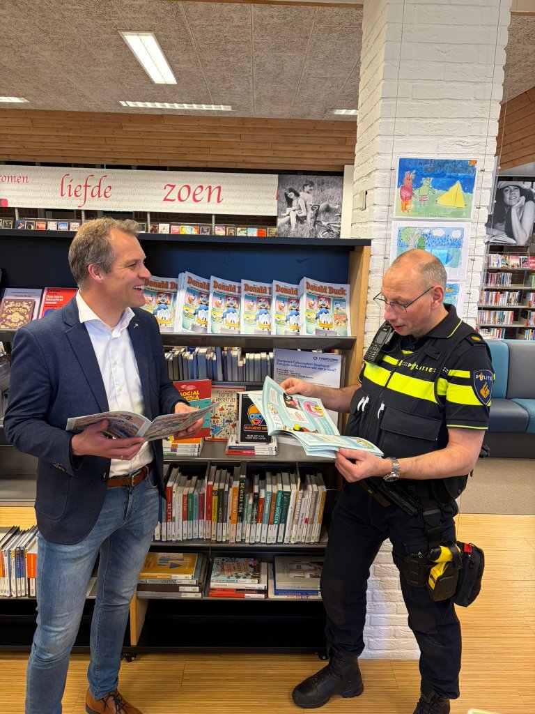 De wethouder en een politieagent bladeren in de bibliotheek door een DigiDuck