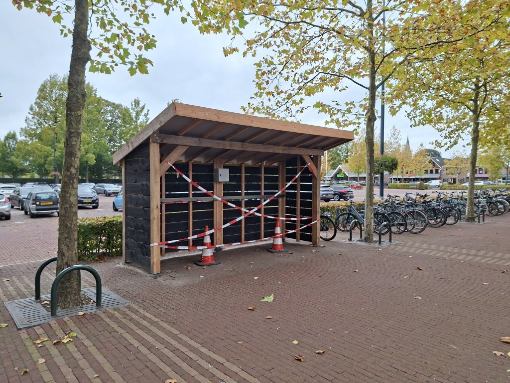 Houten overkapping waar de deelfietsen komen te staan. Het wordt afgeschermd met roodwitte linten.
