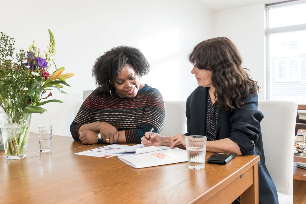 Twee vrouwen zitten aan een tafel en kijken samen naar documenten.