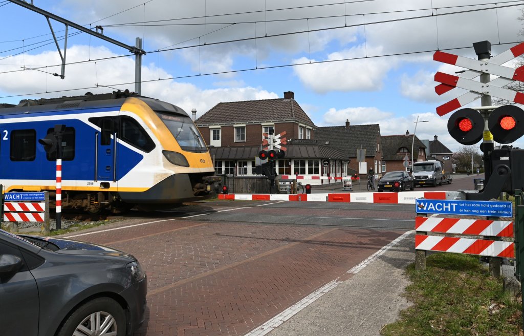 Trein passeert spoorwegovergang. Aan beide kanten staan auto's te wachten.