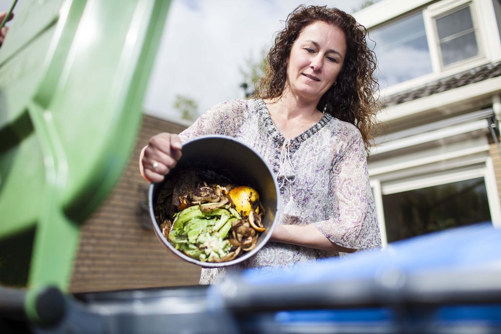 Vrouw gooit gft afval in groene container