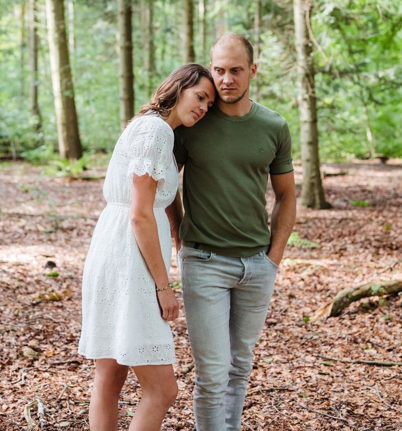 Man en vrouw in het bos, vrouw leunt met gezicht op de schouder van de man.