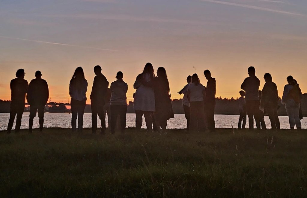 Groep mensen die naar zonsopkomst staan kijken aan de oever van een rivier