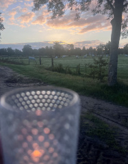 Landweggetje met aan de horizon een opkomende zon. Vooraan brandt een kaars in een glazen windlichtje.