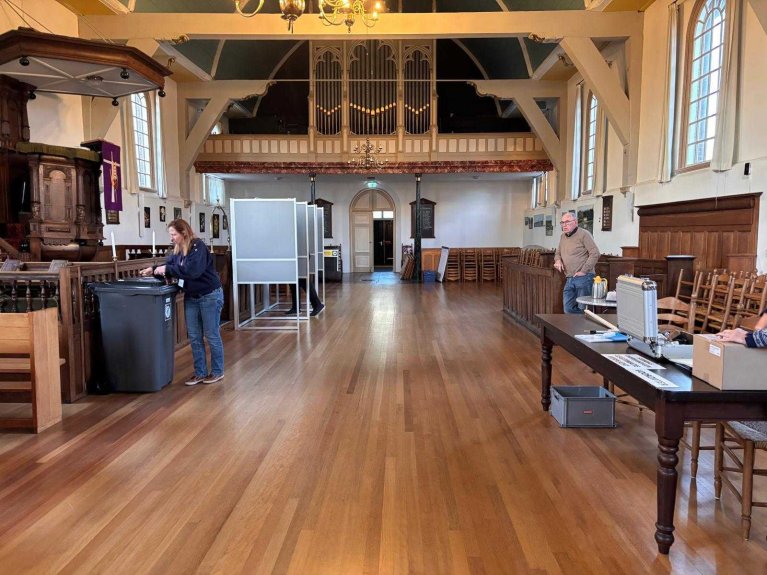 Binnen in de kerk. Links staan de stemhokjes, rechts de leden van het stembureau.