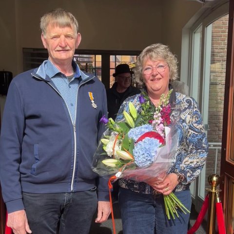 Echtpaar op rode loper voor de raadzaal met bos bloemen en Koninklijk lintje