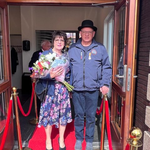 Echtpaar op rode loper voor de raadzaal met bos bloemen en Koninklijk lintje