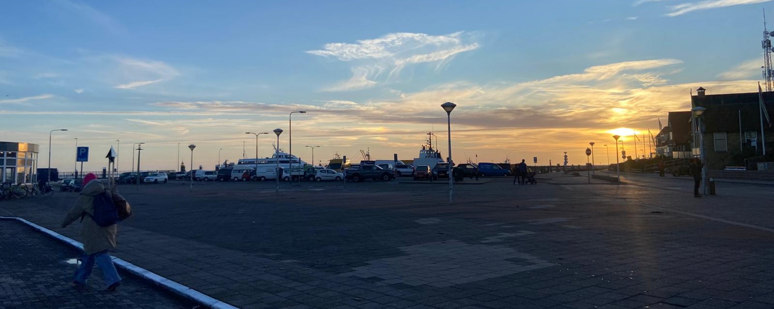 Veerhavenplein bij zonsondergang met geparkeerde auto's in de verte.