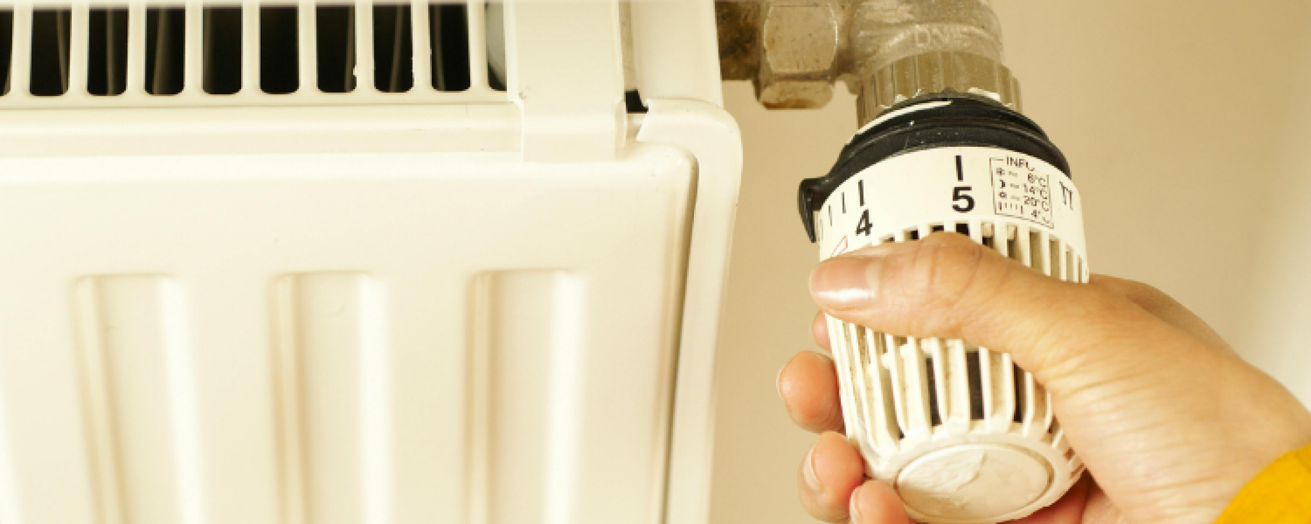 Een radiator waarvan de radiatorknop omlaag gedraaid wordt door een hand.