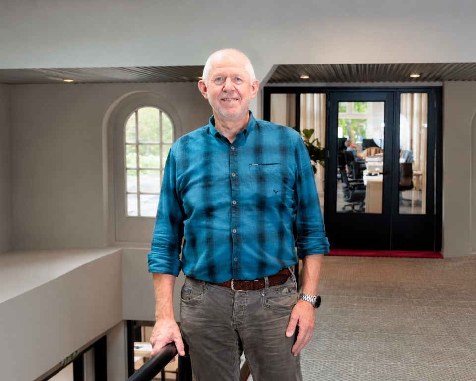 Henk staat in een gebouw en lacht in de camera