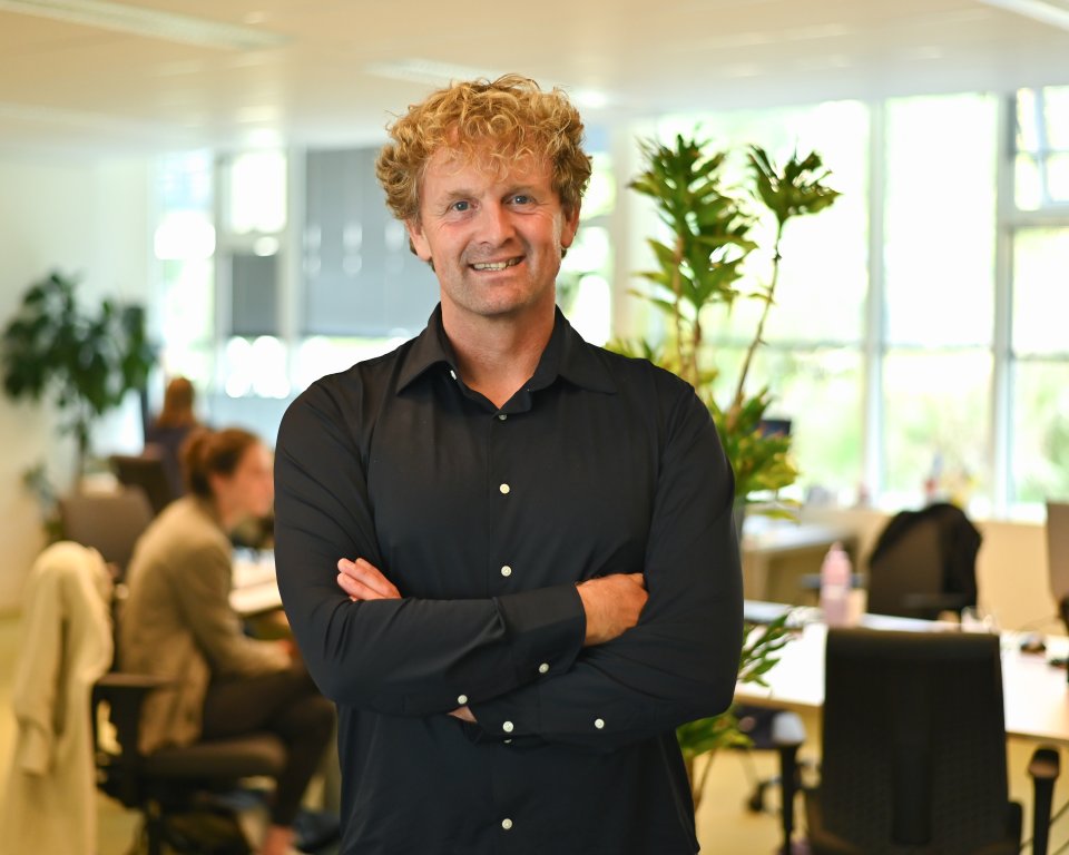 Edzart staat op de werkvloer met zijn handen over elkaar en lacht de camera in.