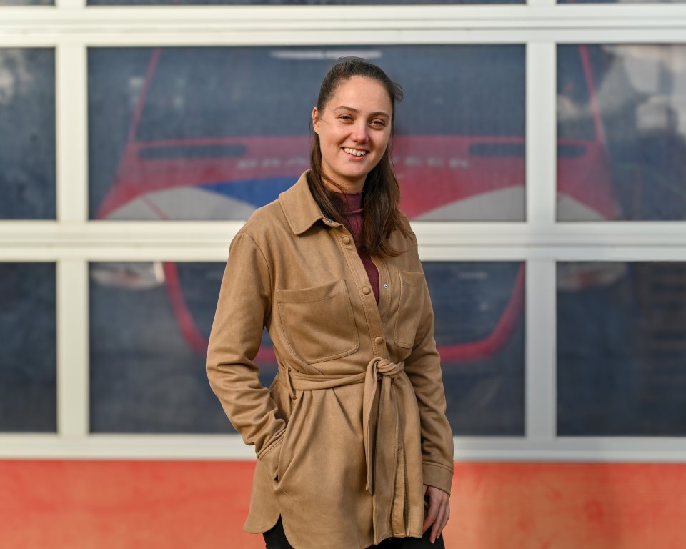 Portretfoto van Ilse voor de deuren van de brandweerkazerne, waar je een brandweerauto doorheen ziet