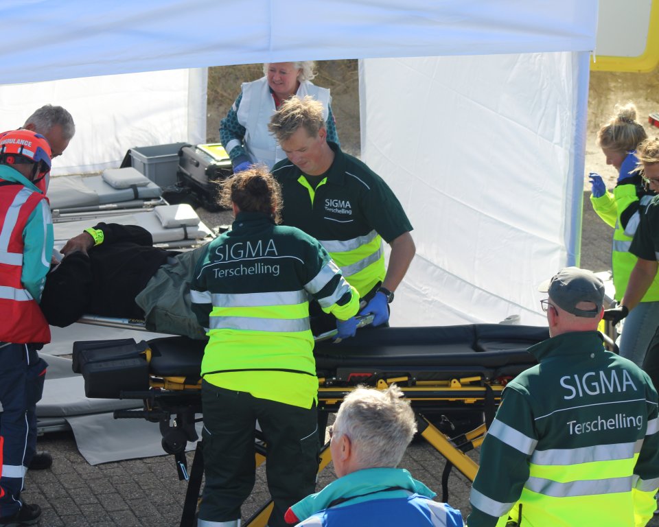 Meerdere vrijwilligers van SIGMA bezig met een oefening. Ze zijn bezig met een leeg brancard.